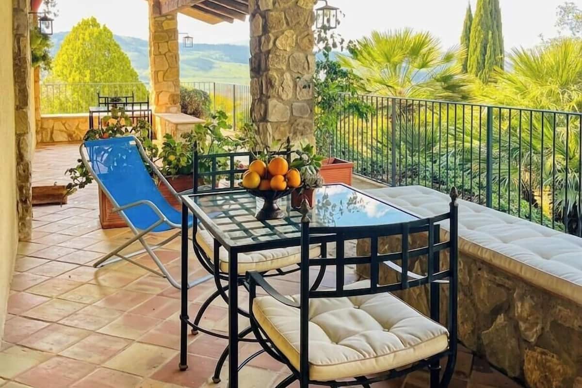 Eine überdachte Terrasse mit Tisch, Stühlen und einem blauen Liegestuhl.
