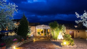 A stone building with a sign reading 'erapatica' at night, surrounded by potted plants and a cobblestone path.
