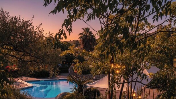 A swimming pool surrounded by lush greenery and trees, with a clear view of the sky.