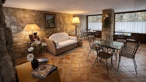 A cozy room with a stone wall, a white sofa, a glass table with chairs, and two floor lamps.