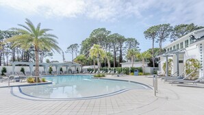 Piscina con sillones de descanso, palmeras y un edificio con terraza cubierta.
