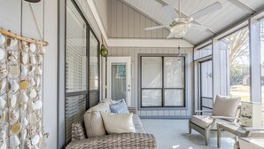 Un porche cubierto con muebles de mimbre, ventilador de techo y pared decorada con conchas marinas.