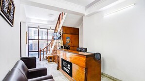 A hotel reception desk with a wooden finish, a staircase, and a view of the city through large windows. - Deluxe Tyagi Road Dehradun Railway Station (Dehradun)