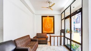A room with a sofa, a chair, a ceiling fan, a window with a view of the outside, and a decorative wall piece. - Deluxe Tyagi Road Dehradun Railway Station (Dehradun)