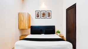 A bedroom with a bed, a wooden cabinet, a dark headboard, a nightstand with a plant, and three framed leaf artworks on the wall. - Deluxe Tyagi Road Dehradun Railway Station (Dehradun)