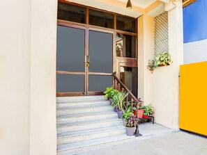 A staircase leading to a wooden door with glass panels, potted plants on the steps, and a yellow wall to the right. - Deluxe Tyagi Road Dehradun Railway Station (Dehradun)