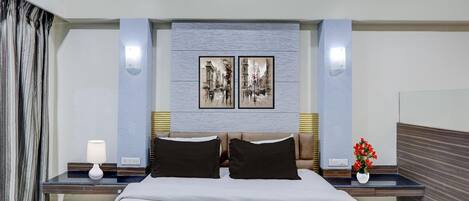 A hotel room with a bed, nightstands, a lamp, a vase with flowers, and two framed pictures on the wall.