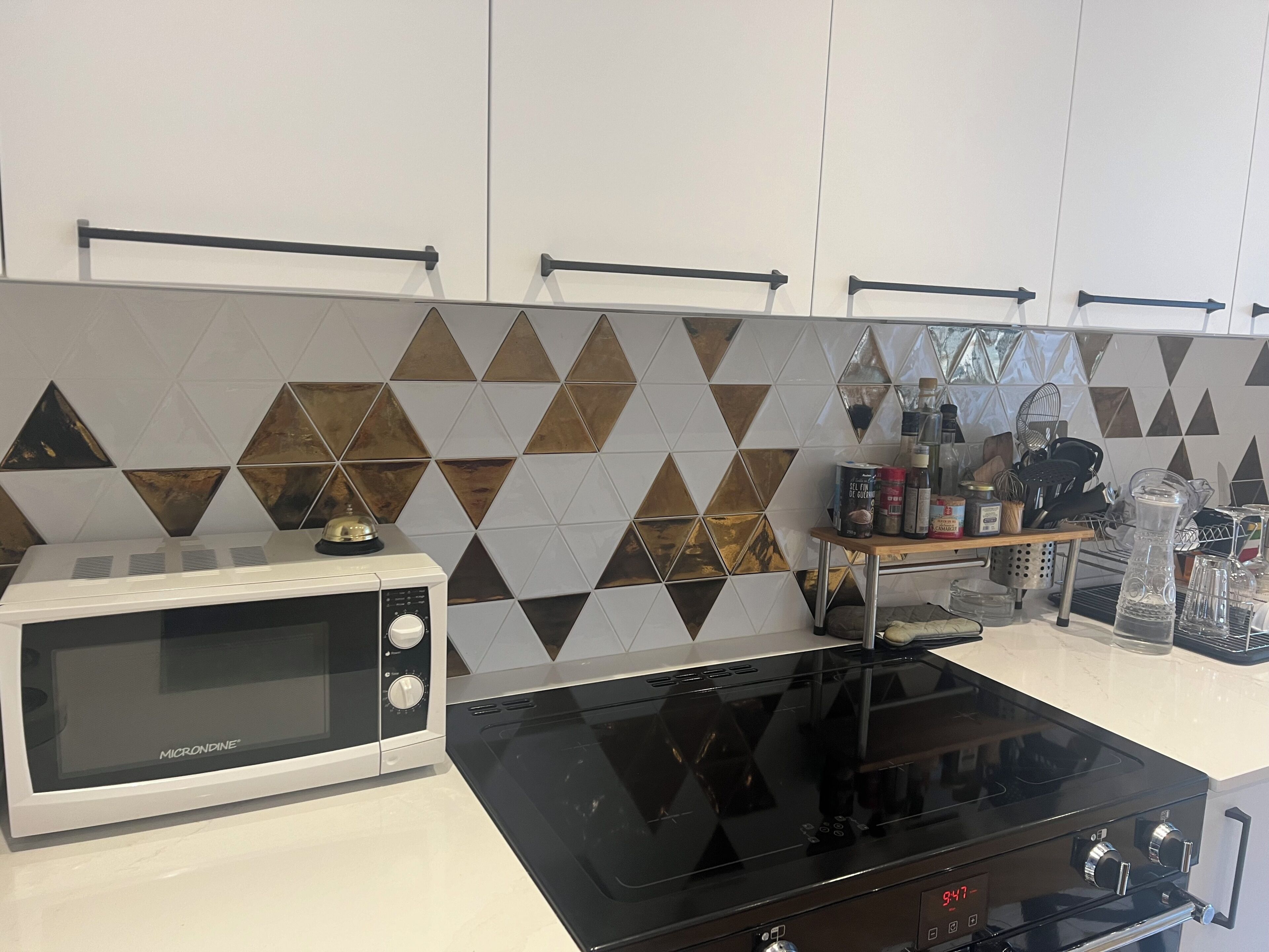 A kitchen with a microwave, stove, and a shelf with kitchen items.