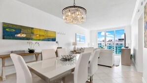 A modern dining area with a chandelier, a large abstract painting, and a view of the city. - Stunning Beachfront Penthouse - Panoramic Ocean Views - 1 Bed / 1 Bath -Paradise (Hollywood)
