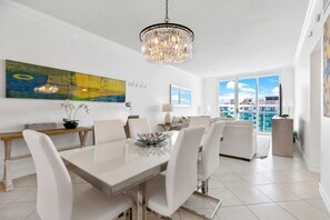 A modern dining area with a chandelier, a large abstract painting, and a view of the city. - Stunning Beachfront Penthouse - Panoramic Ocean Views - 1 Bed / 1 Bath -Paradise (Hollywood)