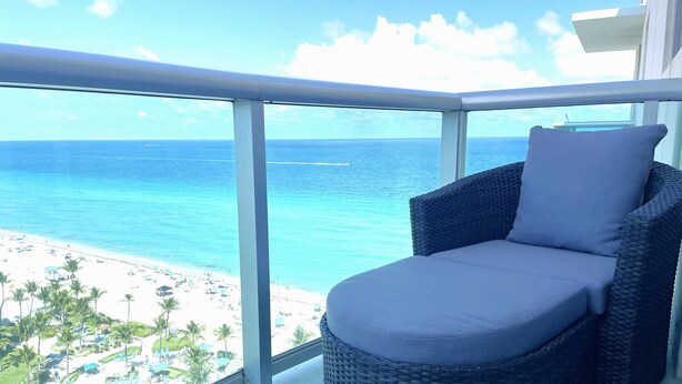 A balcony with a wicker chair and a view of a beach and ocean. - Stunning Beachfront Penthouse - Panoramic Ocean Views - 1 Bed / 1 Bath -Paradise (Hollywood)