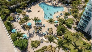 An aerial view of a resort with a swimming pool, palm trees, lounge chairs, and a building with balconies. - Stunning Beachfront Penthouse - Panoramic Ocean Views - 1 Bed / 1 Bath -Paradise (Hollywood)