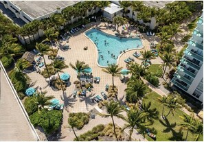 An aerial view of a resort with a swimming pool, palm trees, lounge chairs, and a building with balconies. - Stunning Beachfront Penthouse - Panoramic Ocean Views - 1 Bed / 1 Bath -Paradise (Hollywood)