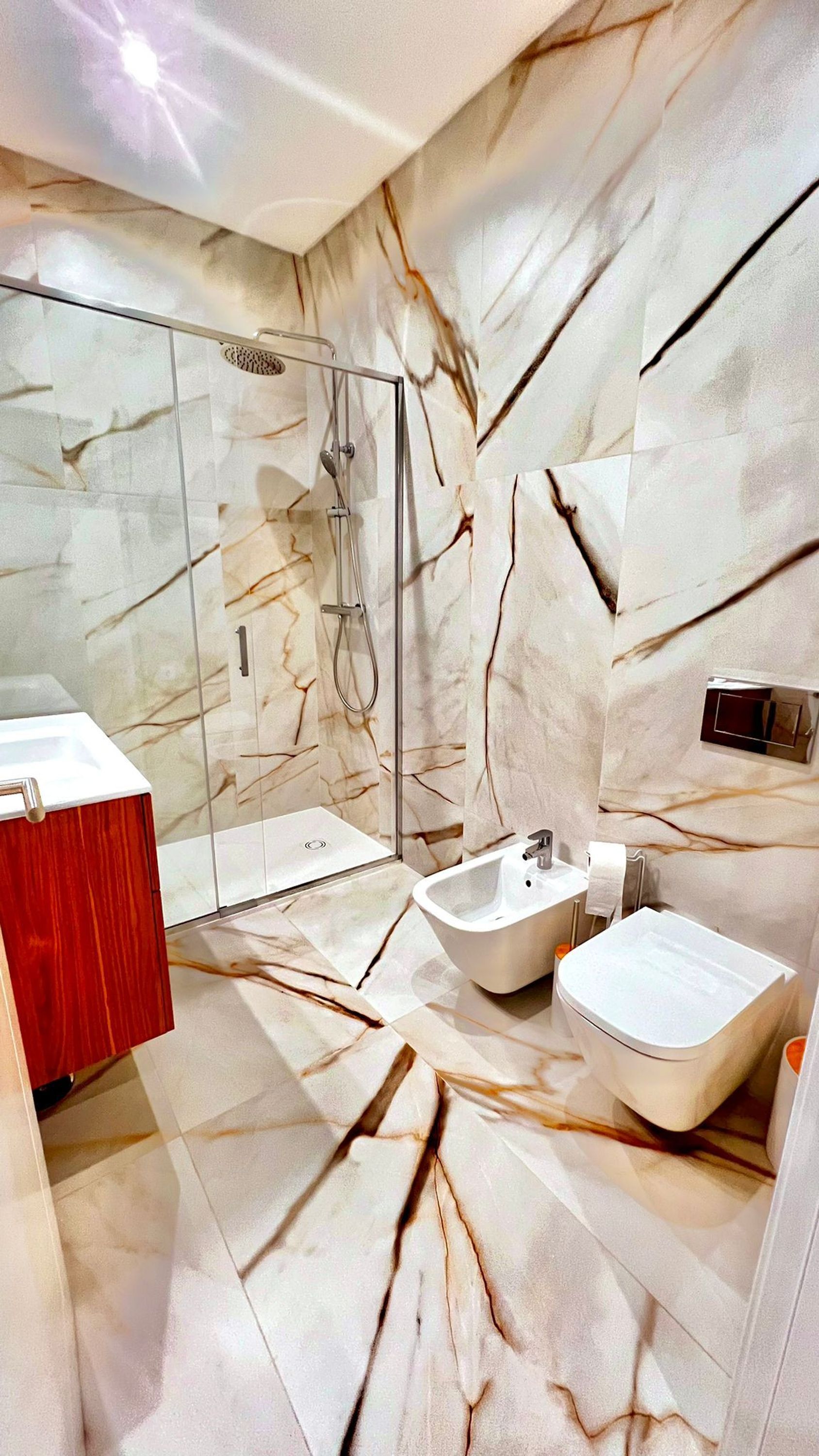 Un baño moderno con salpicadero de mármol, ducha con cerramiento de vidrio, un bidé y un tocador de madera.