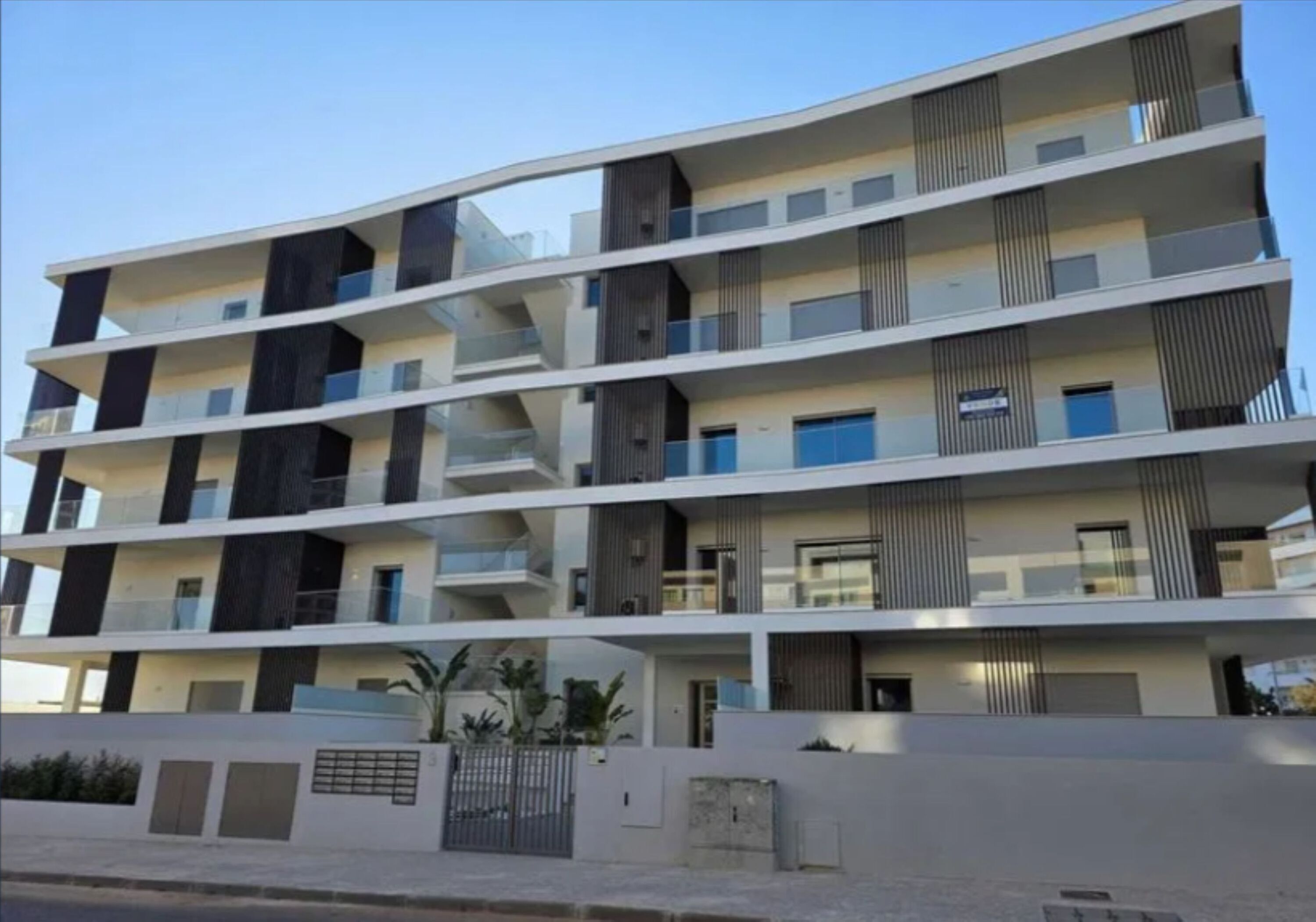 A multi-story residential building with balconies, a gated entrance, and a flat roof.
