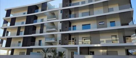 A multi-story residential building with balconies, a gated entrance, and a flat roof.