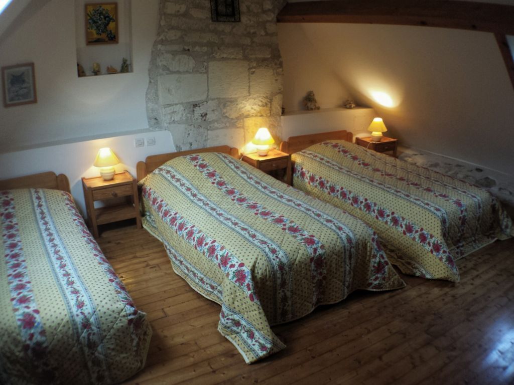 A cozy attic bedroom with three wooden beds, each with a bedside lamp, set against a stone wall.