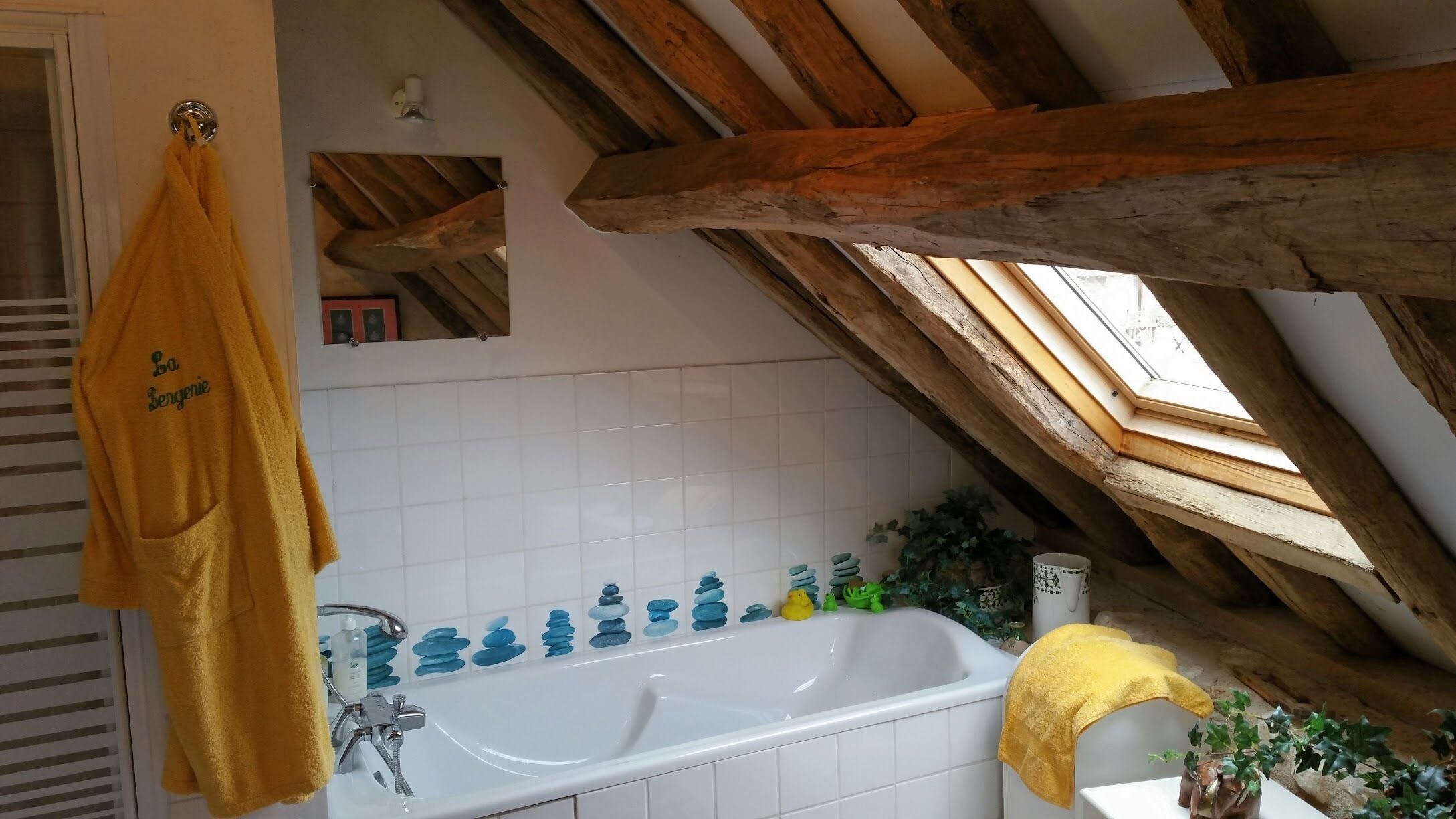 Une salle de bain avec une baignoire, un porte-serviettes, un miroir et une lucarne.