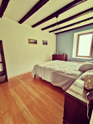 Quarto com cama, piso de madeira e janela.