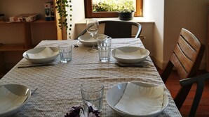 A dining table set with plates, glasses, and a vase of flowers, with a window view of a forest and mountains.