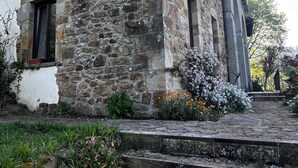 A stone building with a rustic exterior, a set of wooden steps leading to the entrance, and a garden with various plants and flowers.
