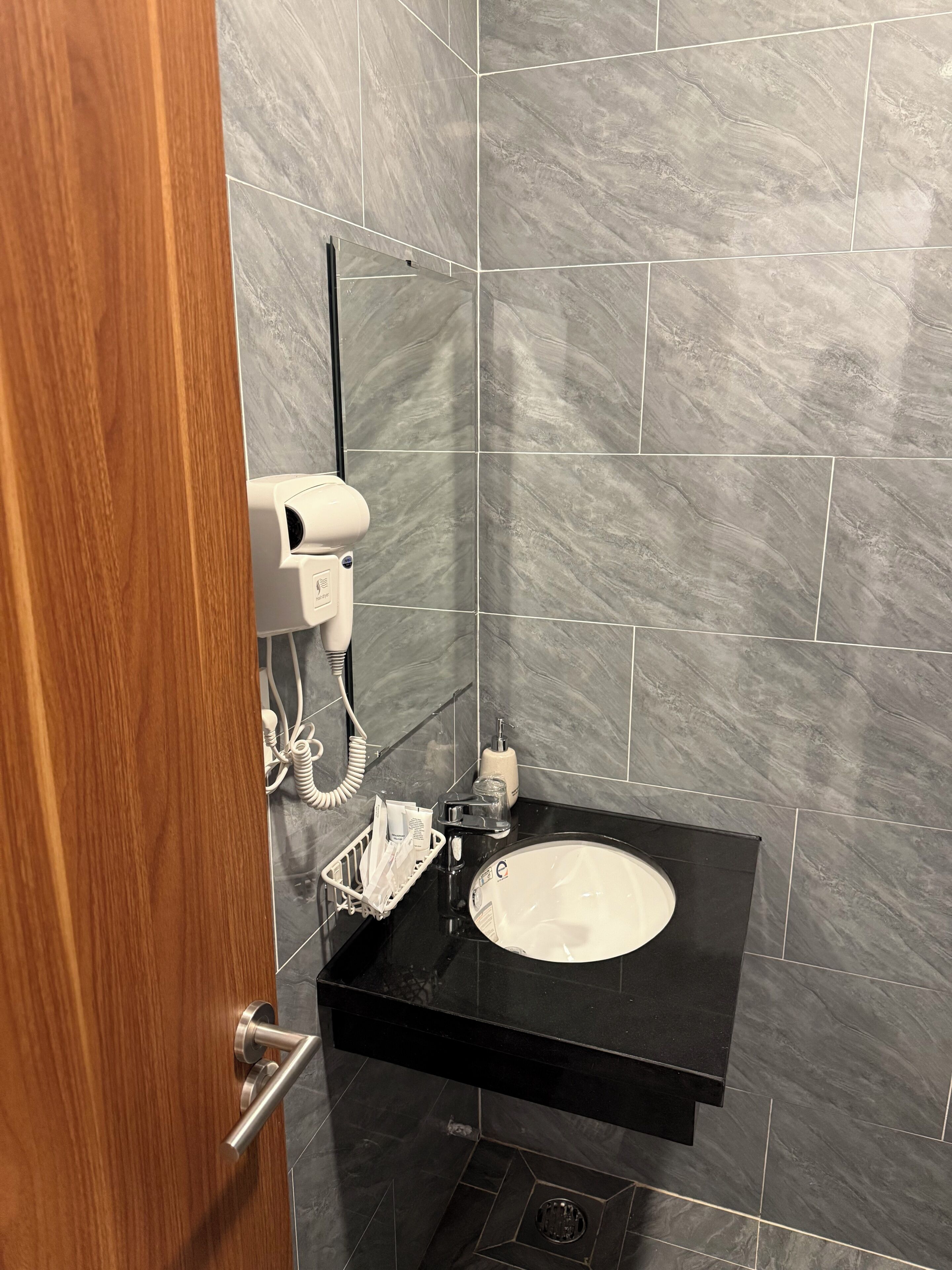 Casa de banho com lavatório preto, secador de cabelo e um frasco de sabonete líquido.