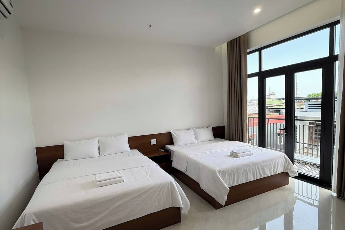 Habitación de hotel con dos camas, un ventanal grande y vista a la ciudad.