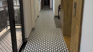 A corridor with patterned flooring, a door on the left, and a wooden panel on the right. - THIÊN PHÚC HOTEL (Nghia Lo)