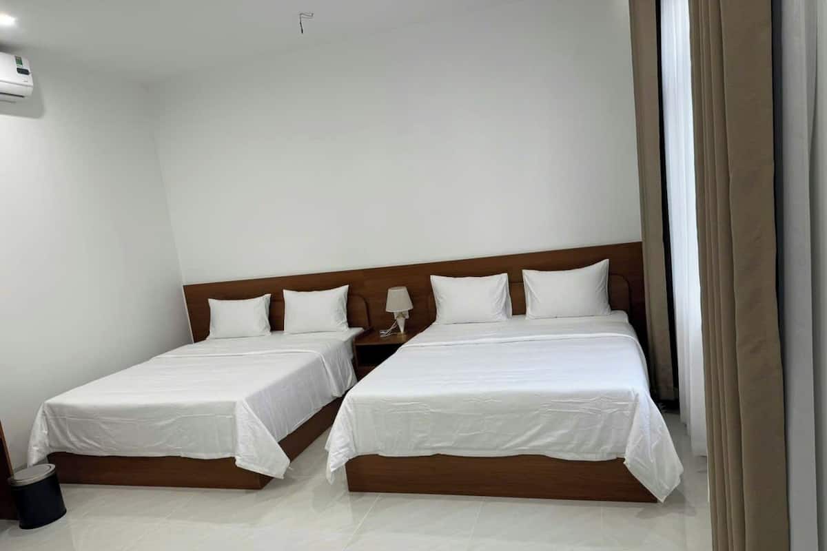 Habitación de hotel con dos camas, una mesita de noche y un aire acondicionado instalado en la pared.