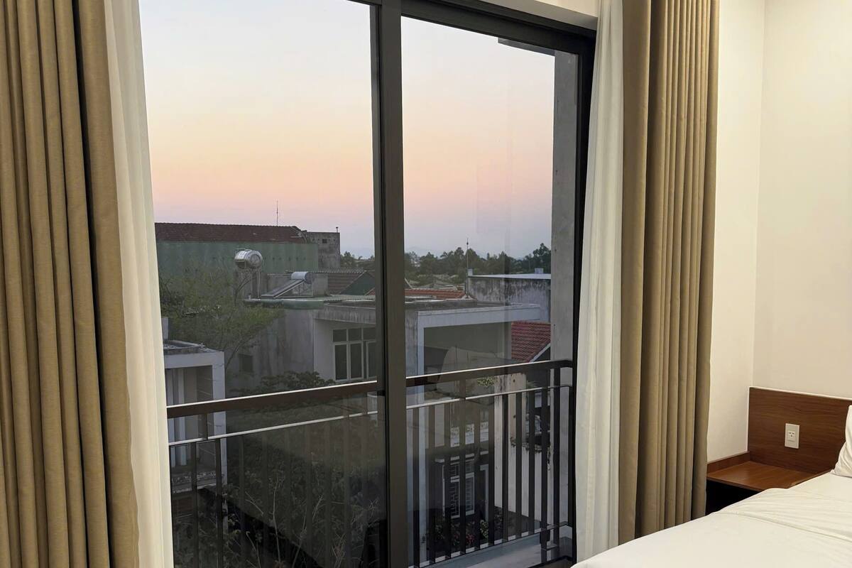 Una habitación de hotel con un ventanal grande, una cama y una mesita de noche.