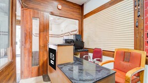 Un espace d’accueil d’hôtel avec un comptoir de réception en bois, un ordinateur, un téléphone et une chaise rouge.