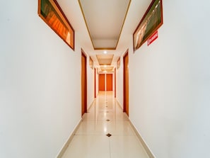 Un long couloir bien éclairé, avec des portes de chaque côté, un panneau indiquant qu’il est interdit de fumer et un sol carrelé.