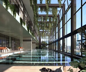 An indoor swimming pool with glass walls, a high ceiling, and hanging plants. - Stylish 2-bed Apartment With Modern Amenities (Melbourne)