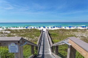 A wooden staircase leading to a beach with blue umbrellas and a sign instructing to place shoes in a rack. - Beach Resort 210 - Scenic Gulf Drive! Massive Lagoon Pool! Step to the Beach! (Miramar Beach)
