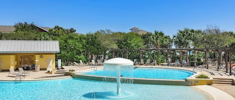A swimming pool with a central fountain, surrounded by lounge chairs and a covered seating area.