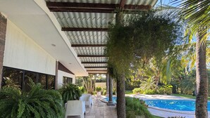 A covered outdoor area with a pool, stone flooring, and greenery. - Villa Privada con Piscina y Vista al Estero (El Zapote)