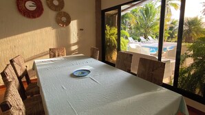 A dining area with a table, chairs, and a view of a pool and palm trees. - Villa Privada con Piscina y Vista al Estero (El Zapote)