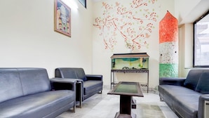 A modern living room with two black leather sofas, a glass-top coffee table, a decorative fish tank, and a wall mural. - Hotel O Tyagi Road Railway (Dehradun)