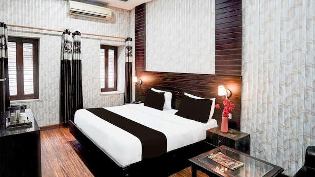 A hotel room with a large bed, a desk, a chair, a nightstand, and a window with curtains. - Hotel O Tyagi Road Railway (Dehradun)