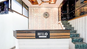 A hotel reception desk with a clock, a staircase with marble steps, and a ceiling fan. - Hotel O Tyagi Road Railway (Dehradun)