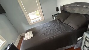 A bedroom with a bed, a nightstand, a window, and a wooden floor. - Arched Haven (Newark)