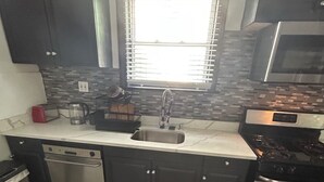 A compact kitchen with a dishwasher, a stove, and a window with blinds. - Arched Haven (Newark)