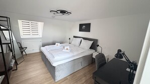 A bedroom with a bed, a desk, a chair, a radiator, and a window with blinds. - 247 Reside: Apartment SZ3 | Center | Netflix (Straubing)