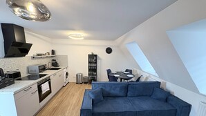 A compact kitchen with modern appliances, a dining area with a table and chairs, and a cozy blue sofa. - 247 Reside: Apartment SZ3 | Center | Netflix (Straubing)