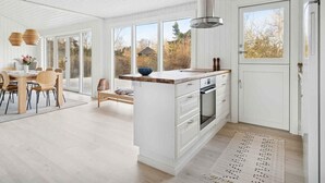 A modern kitchen with a large island, white cabinetry, and a view of the outdoors. - 4 Star Holiday Home in Vaeggerlose (Vaeggerlose)
