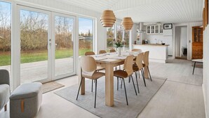 A modern kitchen with white cabinets, a central island, and a dining area with a large table and chairs. - 4 Star Holiday Home in Vaeggerlose (Vaeggerlose)