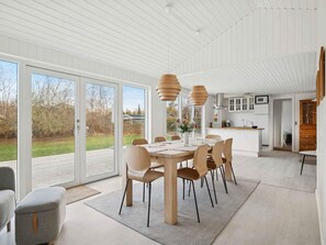 A modern kitchen with white cabinets, a central island, and a dining area with a large table and chairs. - 4 Star Holiday Home in Vaeggerlose (Vaeggerlose)