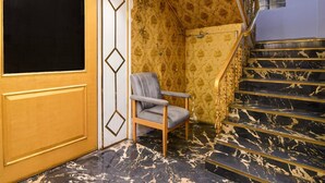Una habitación con una escalera de mármol, una silla y una puerta con diseños geométricos.