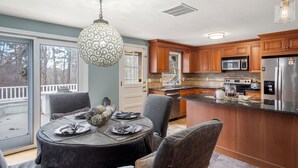 A modern kitchen with wooden cabinets, stainless steel appliances, and a dining area with a round table and chairs. - Modern 2BR Near Gillette Stadium • Private Yard (Sharon)