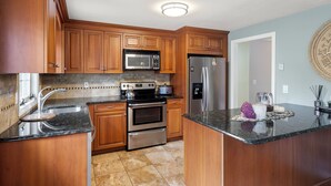 A kitchen with wooden cabinets, stainless steel appliances, a granite countertop, and a clock on the wall. - Modern 2BR Near Gillette Stadium • Private Yard (Sharon)